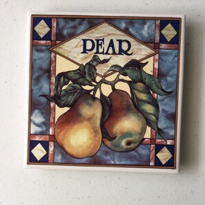 May include: A ceramic tile with a stained glass design featuring two pears on a branch with green leaves. The tile has a yellow background with the word "PEAR" in blue lettering.