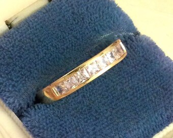 May include: A gold band ring with a row of clear square-shaped stones.