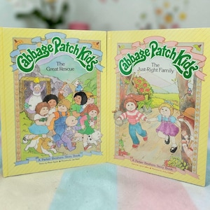 May include: Two vintage Cabbage Patch Kids storybooks. The books have yellow covers with the Cabbage Patch Kids logo in green. The titles are "The Great Rescue" and "The Just-Right Family". The illustrations feature the Cabbage Patch Kids.