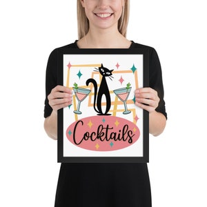 May include: A black cat with a martini glass in each paw sits in front of a pink oval with the word "Cocktails" in black script. The background is a white square with a yellow, blue, and green geometric pattern.