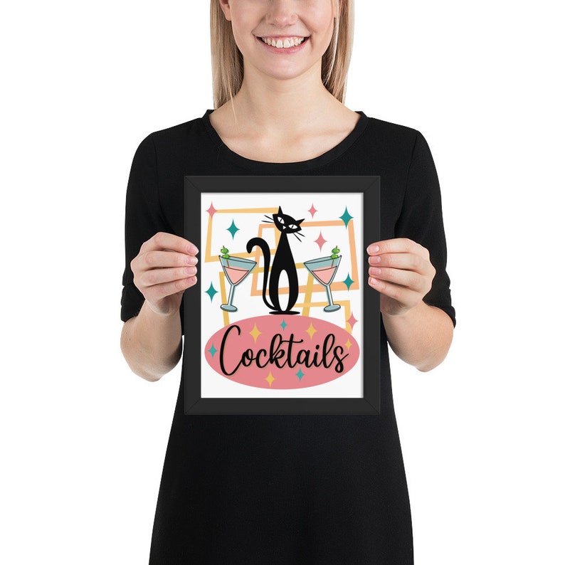 May include: A framed print with a black cat silhouette and two martini glasses. The print has a pink oval with the text "Cocktails" in black script. The background is a retro-style design with yellow, orange, blue, and green colors.