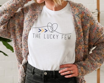 May include: White t-shirt with a black graphic design featuring a heart with three arrows and the text "THE LUCKY FEW".