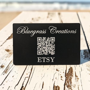 May include: A rectangular black business card featuring the white engraved text Bluegrass Creations at the top, a central square QR code, and the word ETSY printed in white at the bottom. The card has a smooth, matte finish and sharp corners.