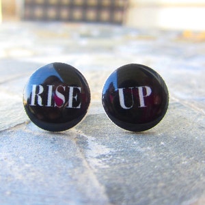 May include: Two black round earrings with white lettering. The left earring says "RISE" and the right earring says "UP".
