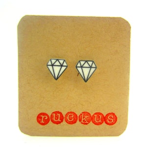 May include: A pair of white diamond-shaped stud earrings with black outlines on a brown card with the word "ruckus" printed in red.