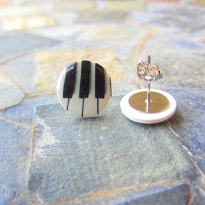 May include: A pair of silver stud earrings with a white background and black piano keys design.