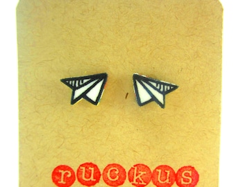 May include: A pair of paper airplane stud earrings on a brown card with the word "ruckus" printed in red.
