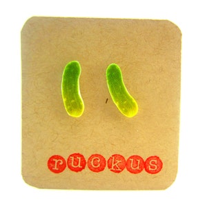 May include: A pair of green and yellow pickle-shaped earrings on a brown card with the word "ruckus" printed in red.