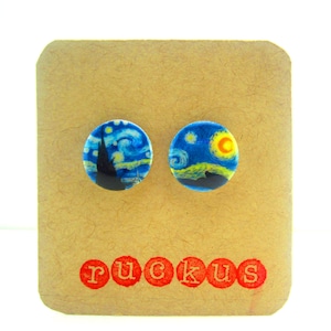 May include: A pair of round, blue and yellow stud earrings with a painting of a starry night sky. The earrings are on a brown card with the word "ruckus" printed in red.