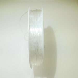 May include: A spool of clear elastic string, wound around a white plastic bobbin.