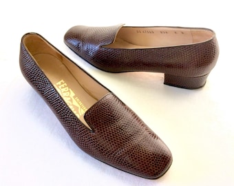 May include: Pair of brown leather loafers with a textured, reptile-like pattern. The shoes have a low heel and a slip-on design. The brand name "Ferragamo" is visible inside one shoe.