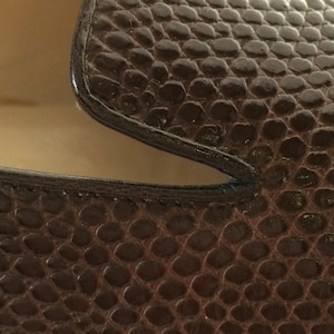 May include: Close-up of a brown leather shoe with a textured, scale-like pattern. The shoe has a dark brown trim and a light tan interior. The focus is on the details of the material and construction.