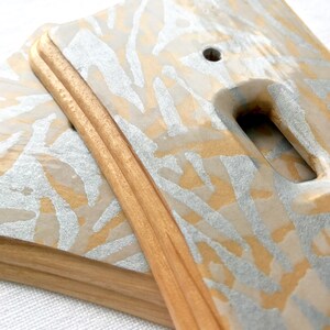May include: Two light switch covers with a wood frame and a white and gold abstract pattern.