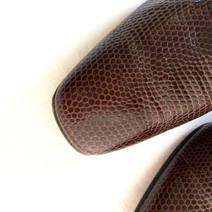 May include: Close-up of two brown leather shoes with a textured, reptile-like pattern. The shoes have a square toe design. The leather is a rich, dark brown color, and the texture creates a unique visual appeal.