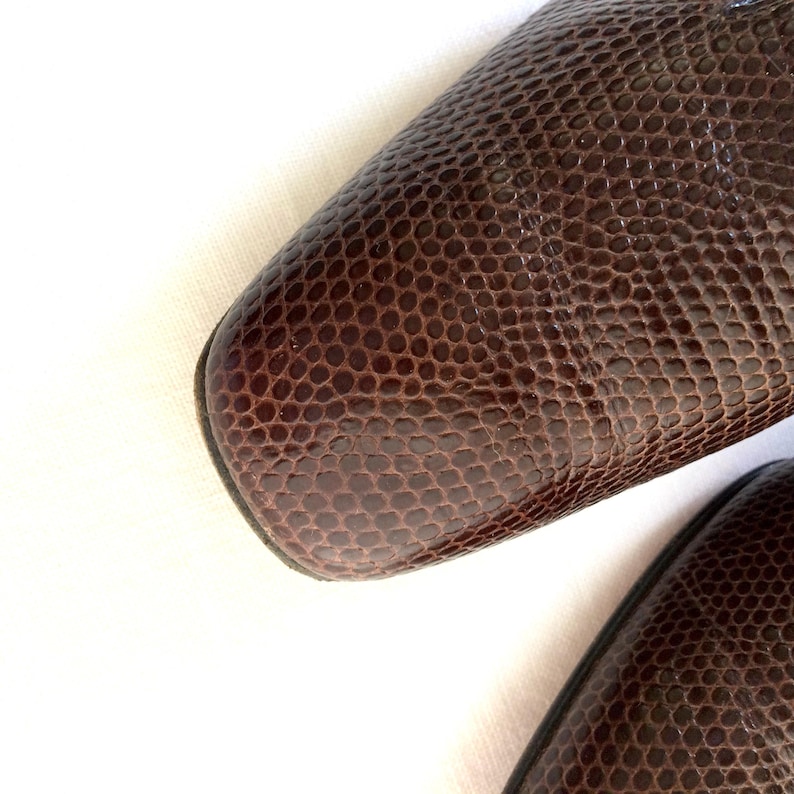 May include: Close-up of two brown leather shoes with a textured, reptile-like pattern. The shoes have a square toe design. The leather is a rich, dark brown color, and the texture creates a unique visual appeal.