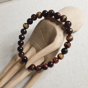May include: A red tiger's eye beaded bracelet with brown and gold accents. The bracelet is made of round beads and is strung on a clear elastic cord.