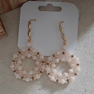 May include: A pair of gold hoop earrings with a delicate white beaded design. The beads are arranged in a circular pattern, creating a delicate and feminine look.