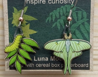 May include: A pair of earrings featuring a green Luna Moth and a green caterpillar on a branch. The earrings are made from cereal box cardboard and are sold by Jabebo Studio, which inspires curiosity.