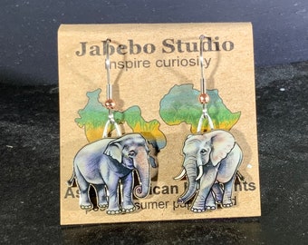 May include: A pair of silver earrings with a copper accent. Each earring features a detailed illustration of an elephant on a white background. The earrings are displayed on a card with the text "Jabebo Studio inspire curiously".