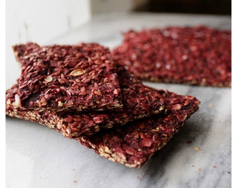 May include: A stack of four rectangular crackers with a dark red hue and a grainy texture. The crackers are covered in small seeds, giving them a speckled appearance.