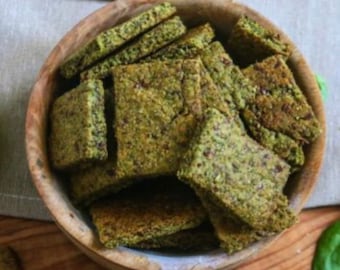 May include: A wooden bowl filled with green and brown crackers. The crackers are rectangular and have a rough texture.