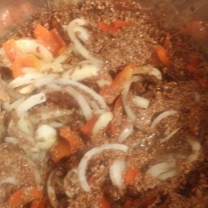 Puede incluir: Primer plano de una olla llena de carne picada cocinada, cebollas y pimientos rojos. Los ingredientes están cocinando a fuego lento en una salsa marrón.