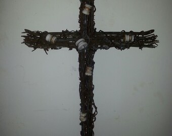 May include: A rustic wooden cross made of barbed wire with white porcelain insulators attached to it.