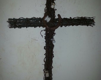 May include: A rustic wooden cross made of branches and barbed wire, decorated with porcelain insulators and a horseshoe.