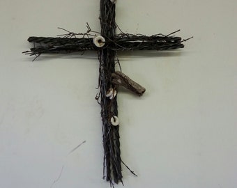 May include: A rustic cross made of barbed wire with white ceramic accents. The cross is mounted on a white wall.
