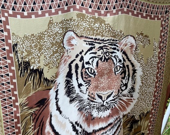 May include: A brown and white tiger with black stripes is printed on a beige silk scarf. The scarf has a brown, black, and green border with a geometric pattern.