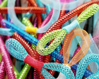 May include: A collection of colorful, glittery mesh tubing craft supplies. The flexible, hollow tubes feature a diamond-patterned texture and are available in vibrant shades including lime green, orange, blue, red, pink, and white, secured with felt.
