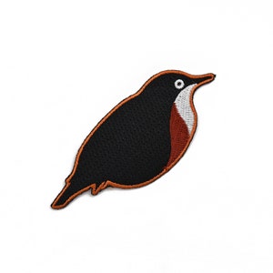 Puede incluir: Parche bordado de pájaro negro y naranja con un ojo blanco.