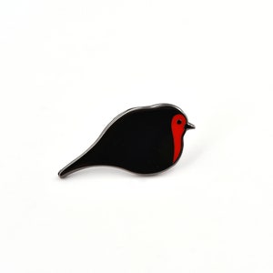 May include: A black enamel pin shaped like a robin with a red breast.