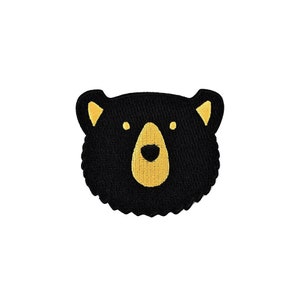 Pode incluir: Patch de rosto de urso preto com detalhes amarelos. O urso tem uma pelagem preta e um nariz e olhos amarelos.