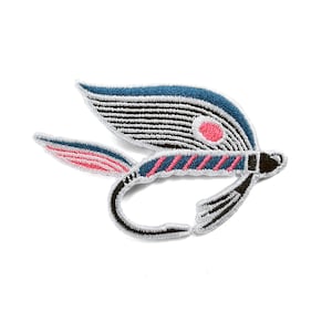 May include: Embroidered patch of a fly fishing lure. The lure has a blue wing with black stripes, a pink dot, and a pink and blue body. The hook is black and white, set against a white background.