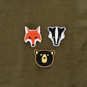 Könnte beinhalten: Drei gestickte Bügelbilder mit einem Fuchs, einem Dachs und einem Bären. Der Fuchs ist orange, der Dachs ist schwarz-weiß und der Bär ist schwarz.