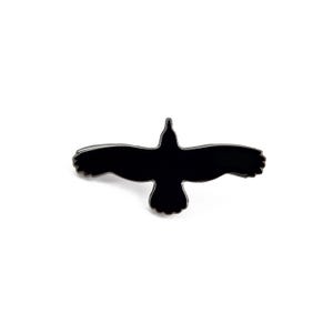 Könnte beinhalten: Ein schwarzer Emaille-Pin in Form eines Vogels im Flug. Der Pin hat eine glänzende schwarze Oberfläche mit silberfarbenen Konturen. Die Flügel des Vogels sind weit ausgebreitet, das Design vor weißem Hintergrund.
