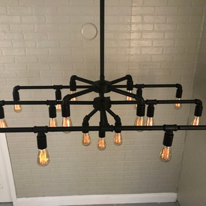 May include: A black metal pipe chandelier with 10 light bulbs. The chandelier is hanging from the ceiling and has a rustic industrial style.