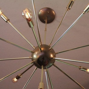 May include: A gold-toned Sputnik-style chandelier with multiple arms extending outward from a central sphere. Each arm has a light bulb at the end.