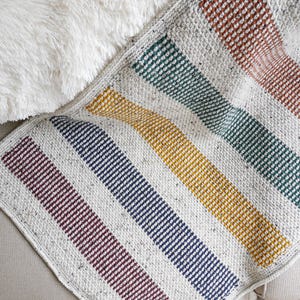 May include: A white crocheted blanket with stripes of burgundy, navy blue, mustard yellow, and teal.