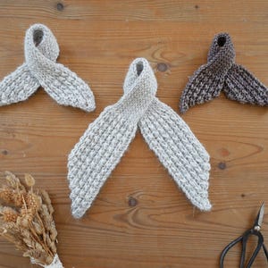 Puede incluir: Tres bufandas tejidas a mano en tonos grises y marrones est&aacute;n dispuestas sobre una superficie de madera. Las bufandas tienen un dise&ntilde;o en bucle. Tambi&eacute;n se ven un peque&ntilde;o ramo de flores secas y unas tijeras.