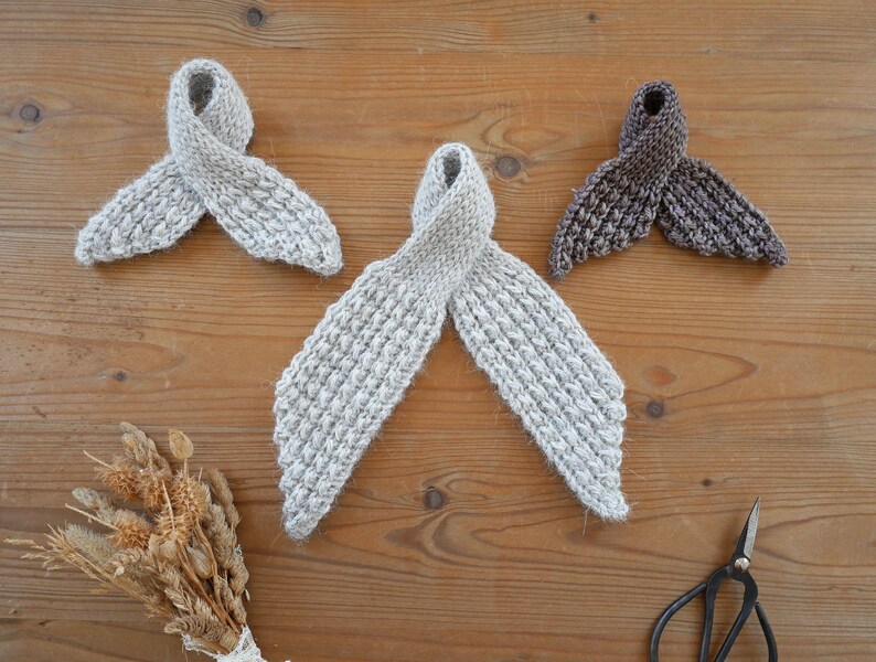 Puede incluir: Tres bufandas tejidas a mano en tonos grises y marrones est&aacute;n dispuestas sobre una superficie de madera. Las bufandas tienen un dise&ntilde;o en bucle. Tambi&eacute;n se ven un peque&ntilde;o ramo de flores secas y unas tijeras.