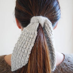 Puede incluir: Una goma para el pelo de punto gris claro asegura una cola de caballo. La goma para el pelo est&aacute; hecha de un hilo suave y texturizado y est&aacute; envuelta alrededor de la base de la cola de caballo. El cabello es una mezcla de colores marr&oacute;n y casta&ntilde;o. La persona lleva un jersey marr&oacute;n.