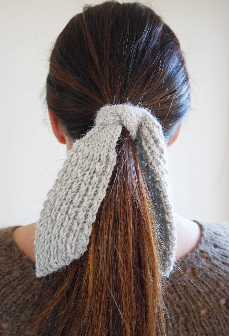 Puede incluir: Una goma para el pelo de punto gris claro asegura una cola de caballo. La goma para el pelo est&aacute; hecha de un hilo suave y texturizado y est&aacute; envuelta alrededor de la base de la cola de caballo. El cabello es una mezcla de colores marr&oacute;n y casta&ntilde;o. La persona lleva un jersey marr&oacute;n.