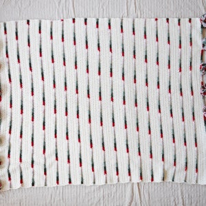 May include: White crochet blanket with red and green stripes and pom-pom trim.