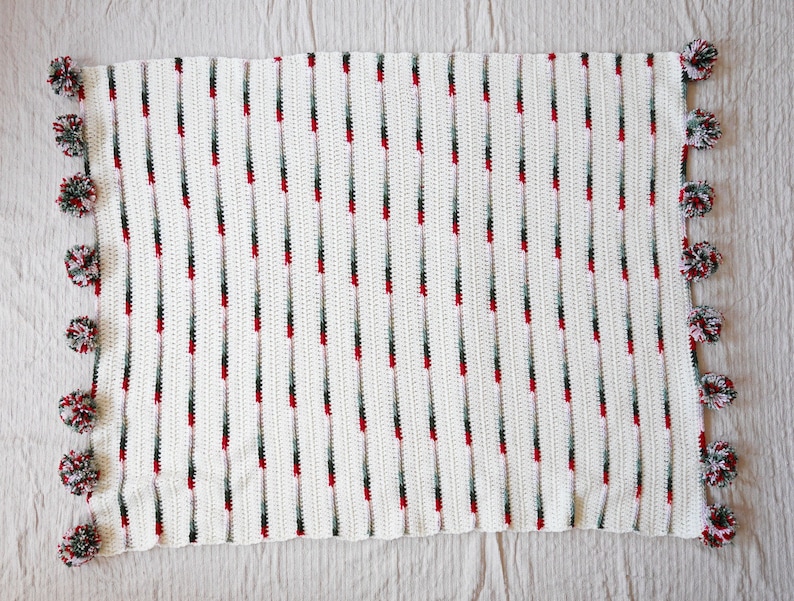 May include: White crochet blanket with red and green stripes and pom-pom trim.