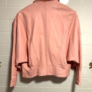 Puede incluir: Una chaqueta de cuero rosa con cuello y mangas largas. La chaqueta tiene una silueta ajustada y una longitud recortada.