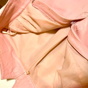 Puede incluir: Una chaqueta de cuero rosa con cierre de cremallera. La chaqueta est&aacute; abierta y el forro es visible.
