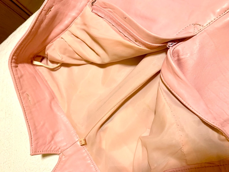 Puede incluir: Una chaqueta de cuero rosa con cierre de cremallera. La chaqueta est&aacute; abierta y el forro es visible.