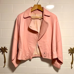 Puede incluir: Una chaqueta de cuero rosa con cierre de cremallera y mangas largas. La chaqueta tiene un estilo motero cl&aacute;sico con un corte ligeramente recortado.